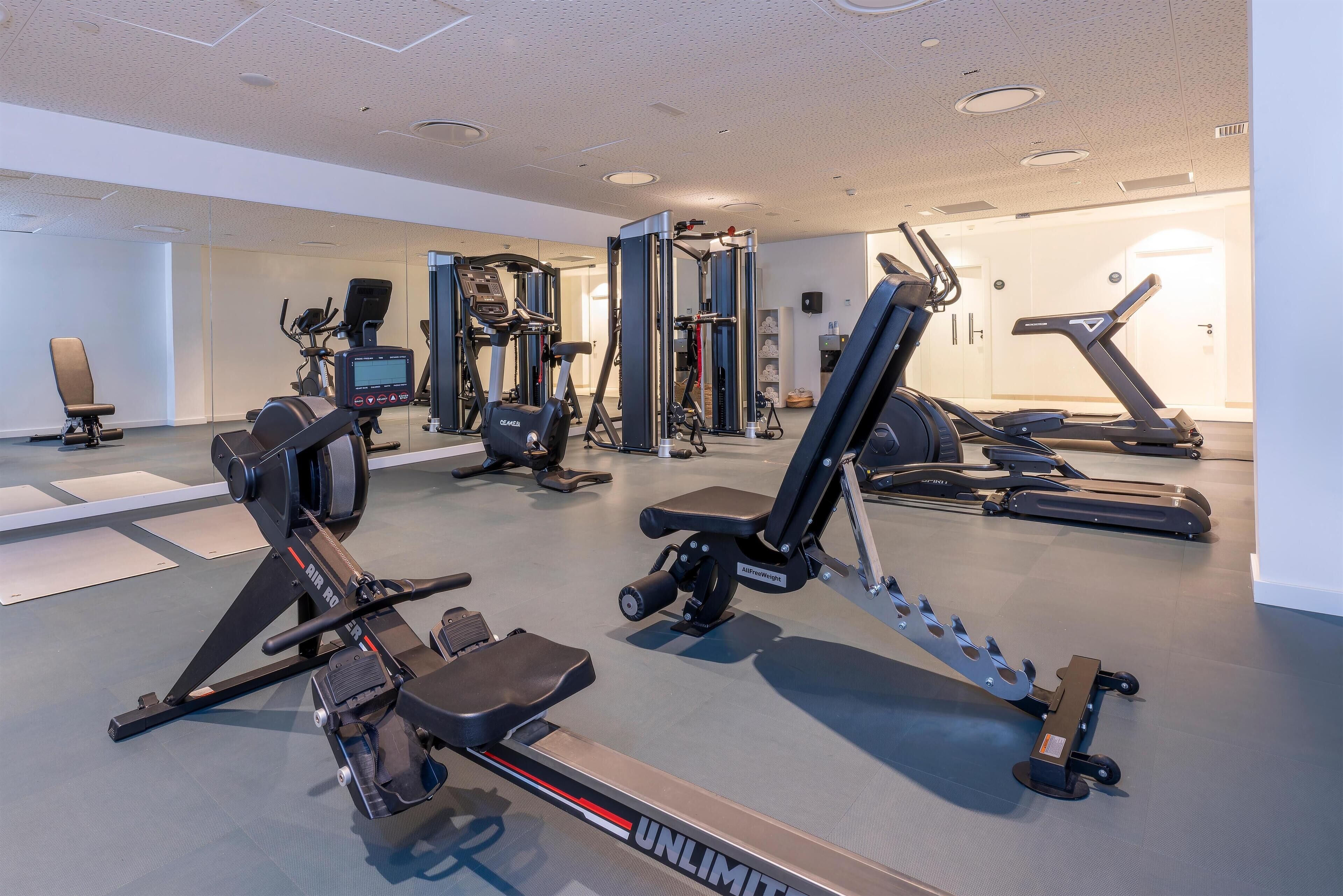 A modern gym with various exercise equipment including treadmills, a rowing machine, and weight machines.