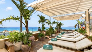 Una terraza en la azotea con sillones de descanso, plantas en macetas y vistas al mar.
