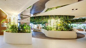 A modern lobby with curved white planters filled with greenery, a high ceiling with exposed ductwork, and a seating area in the background. - Aubamar Palma Resort (Palma de Mallorca)