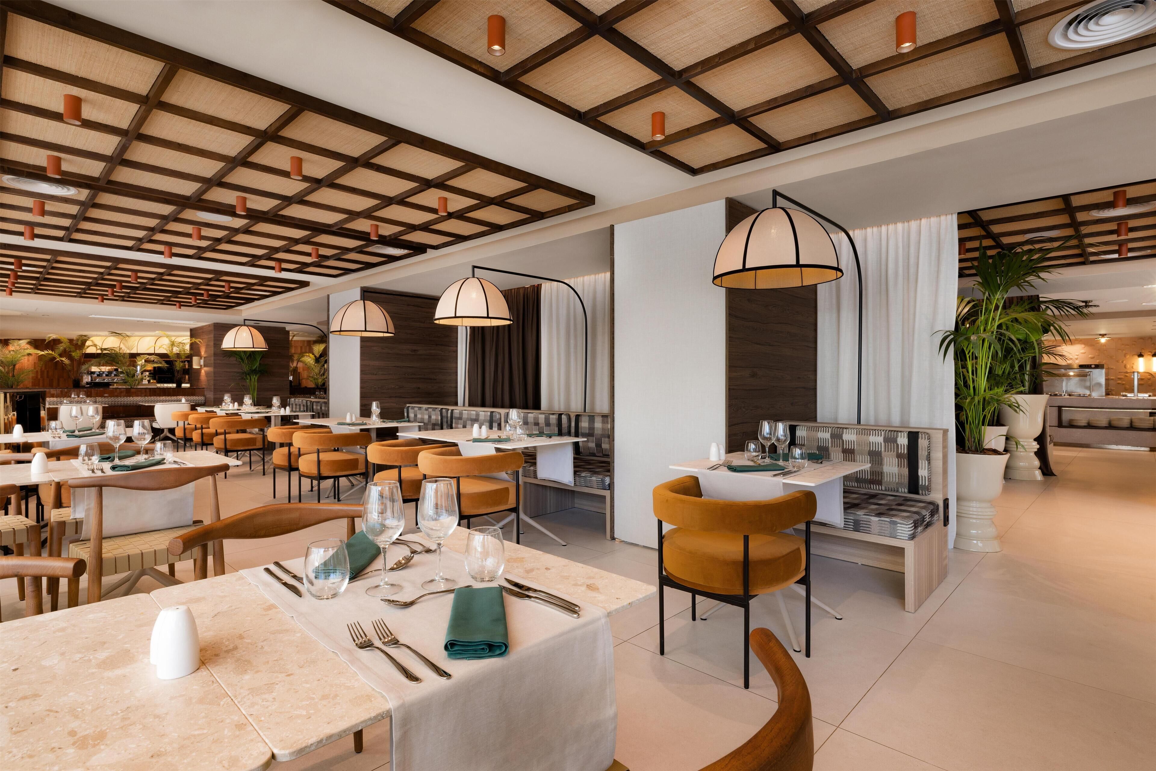 A modern restaurant with wooden ceiling beams, round tables, and orange chairs.