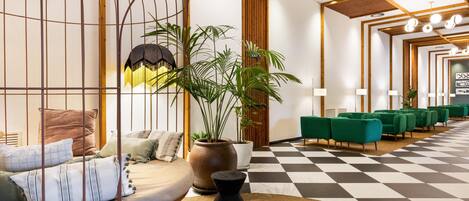 Un hall d'entrée moderne avec un sol à carreaux, des canapés verts, une grande plante en pot et un mur décoratif en bois.