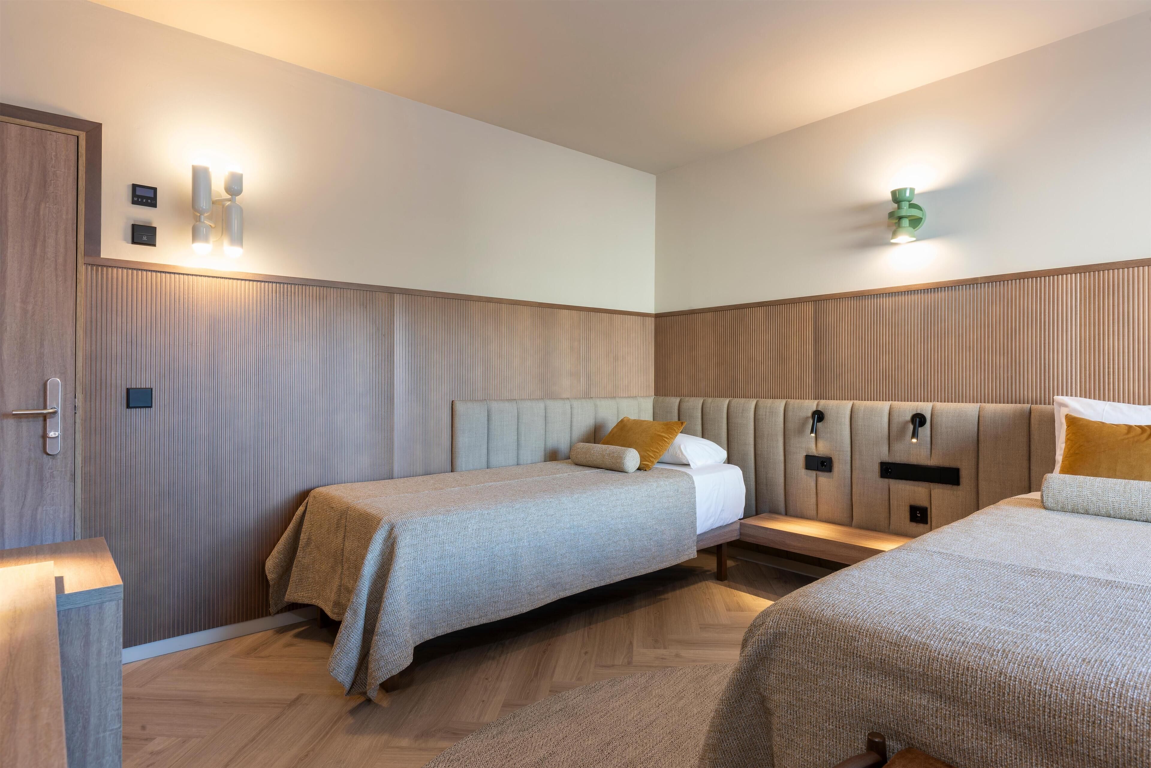 Une chambre d’hôtel avec deux lits, une armoire en bois et un luminaire fixé au mur.