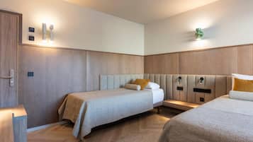 A hotel room with two beds, a wooden wardrobe, and a wall-mounted light fixture.