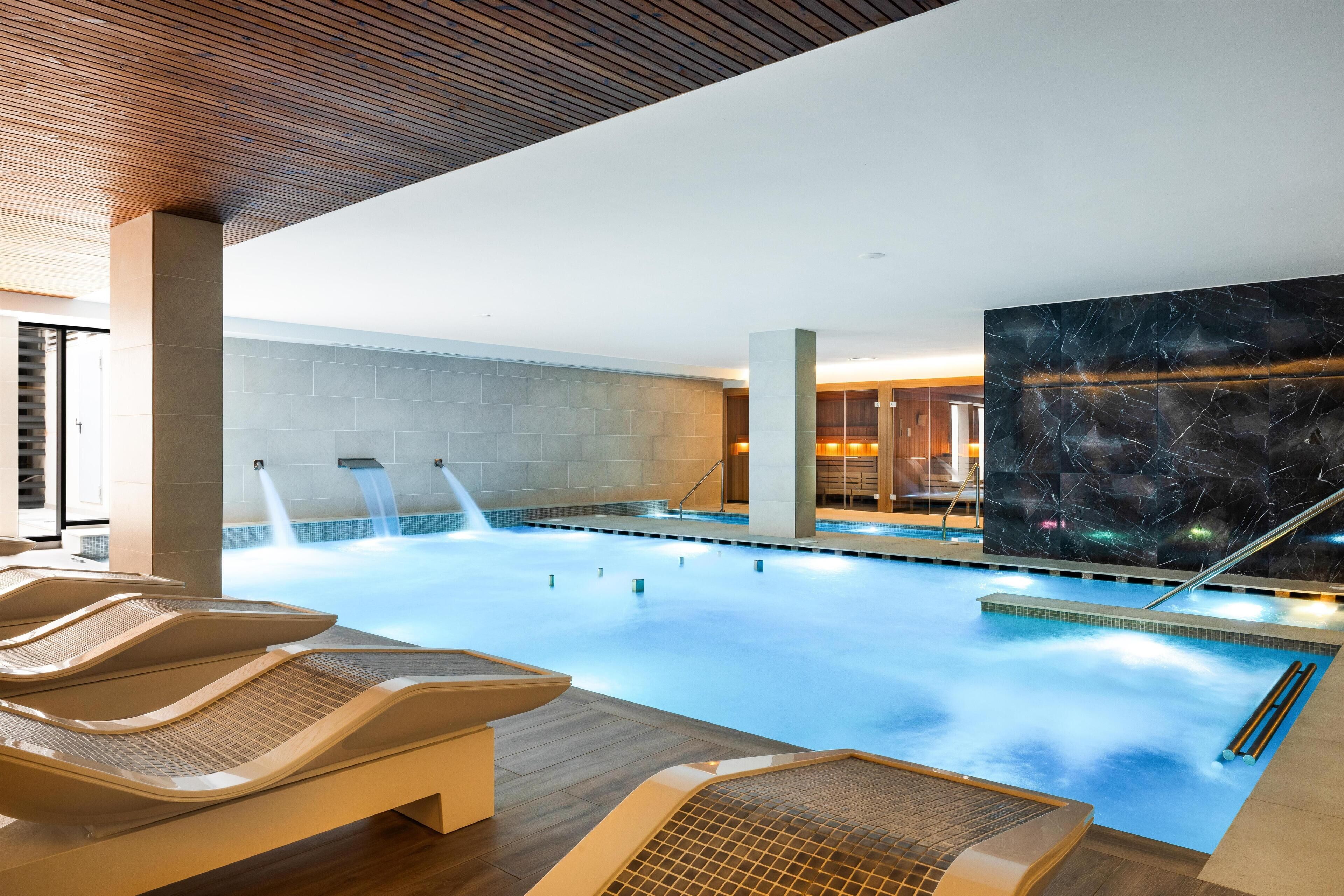 Une piscine intérieure moderne, avec une eau cristalline, un plafond en bois et un grand mur de marbre.