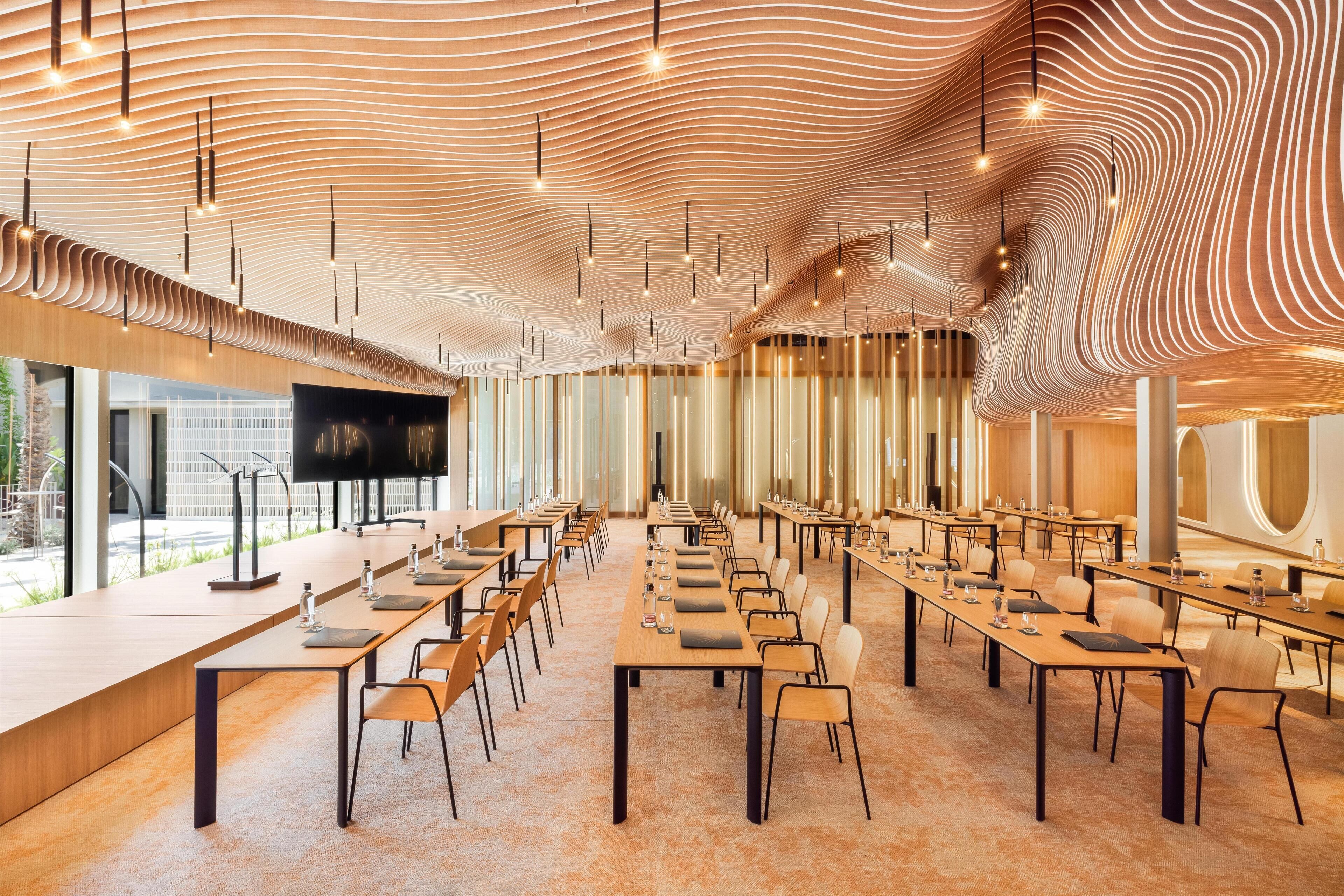 A conference room with long tables, chairs, and a large screen.