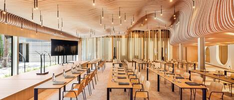 A conference room with long tables, chairs, and a large screen.
