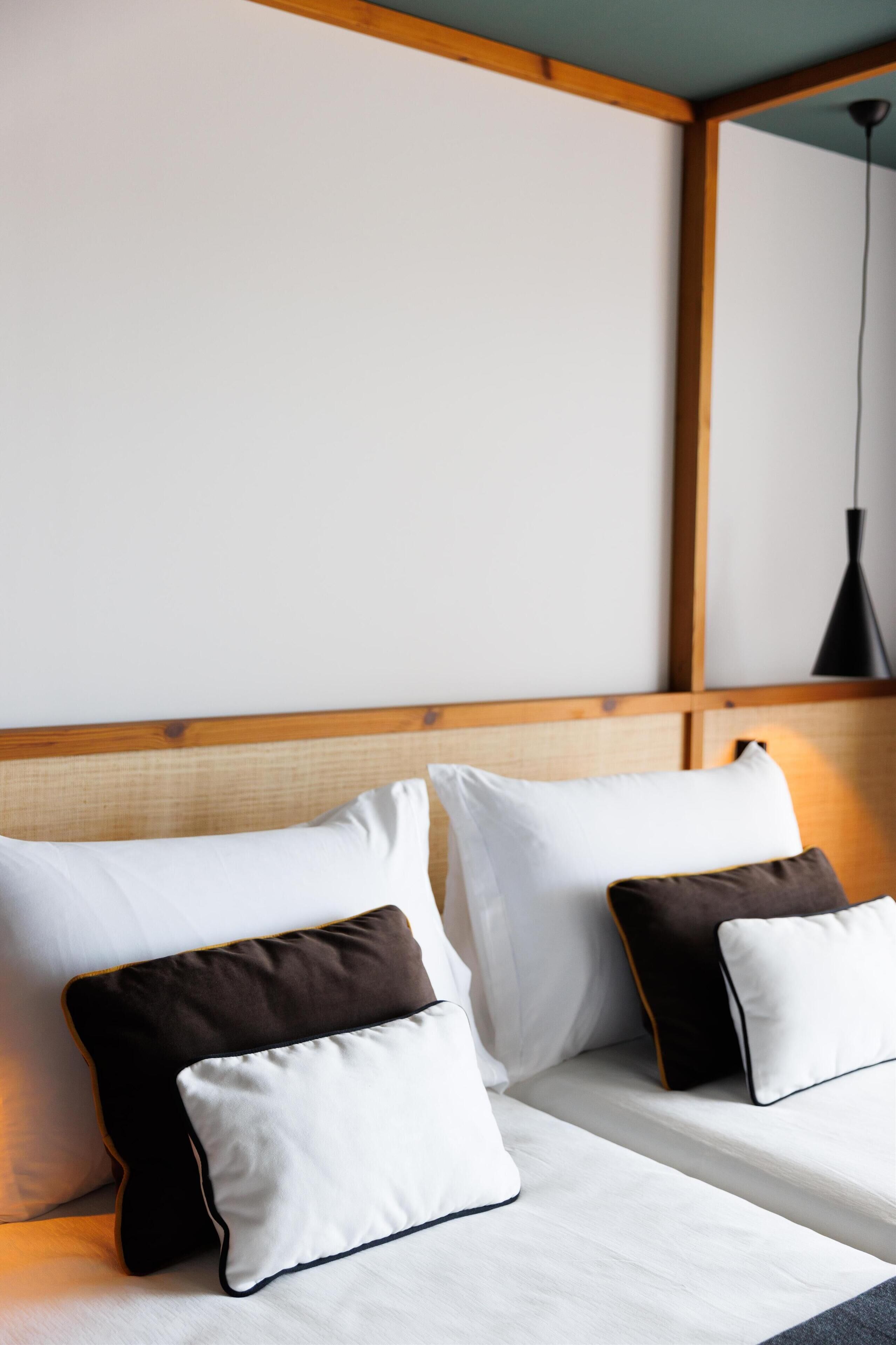 Un lit avec des oreillers blancs et bruns, une tête de lit en bois et une lampe suspendue.
