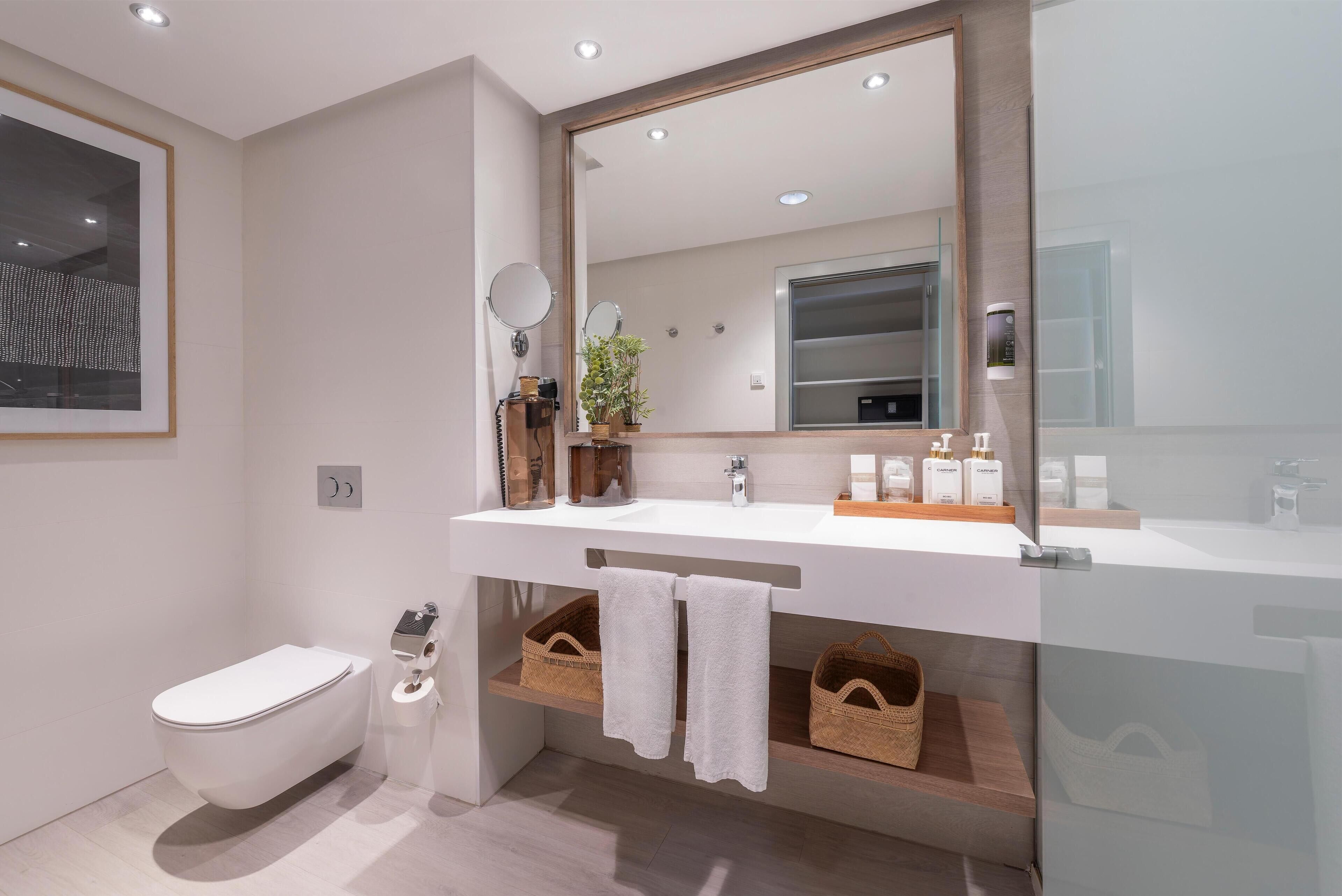 A modern bathroom with a white toilet, a large mirror, and a white sink.