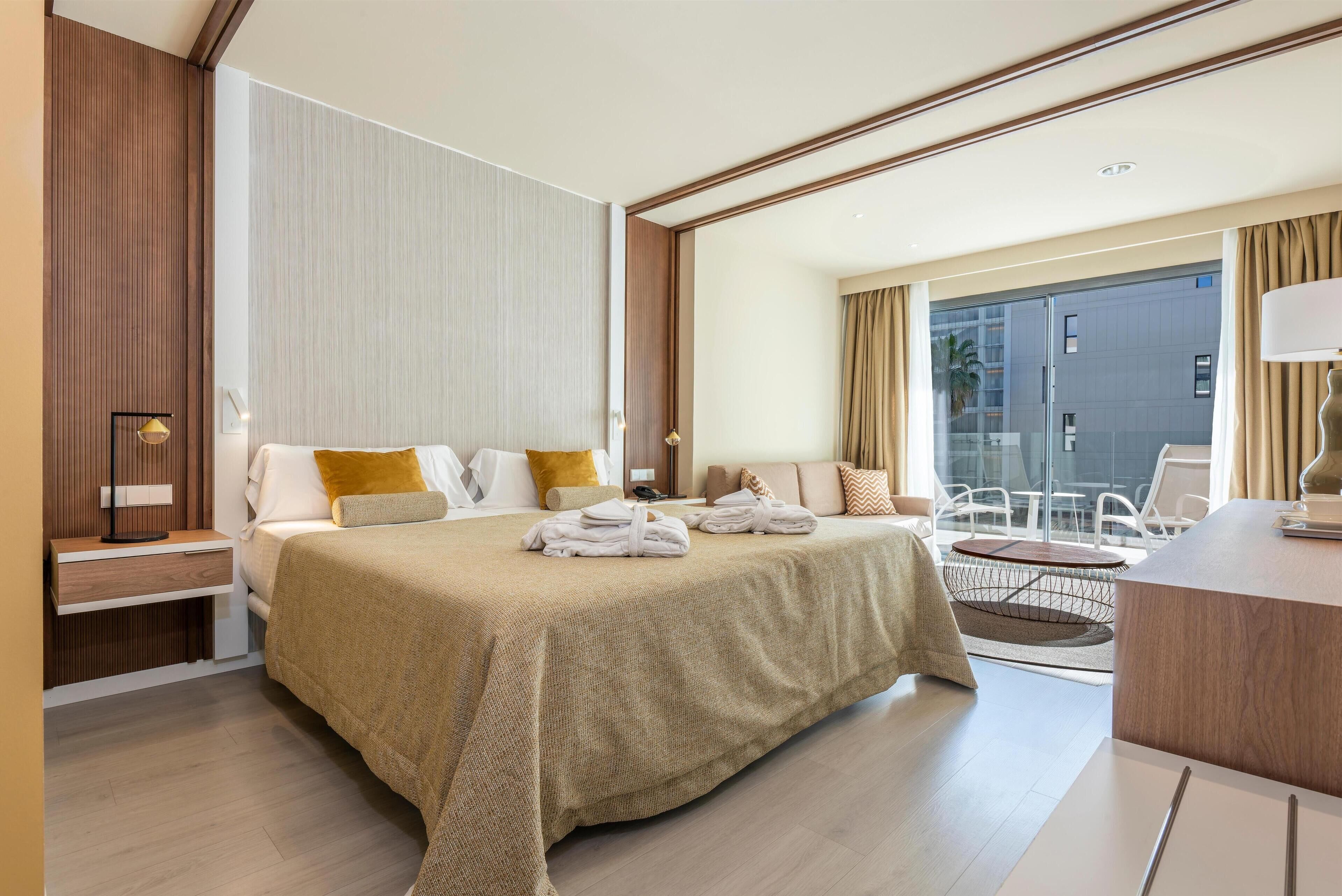 Una habitación de hotel moderna con una cama grande, un escritorio y un balcón con vistas a la ciudad.