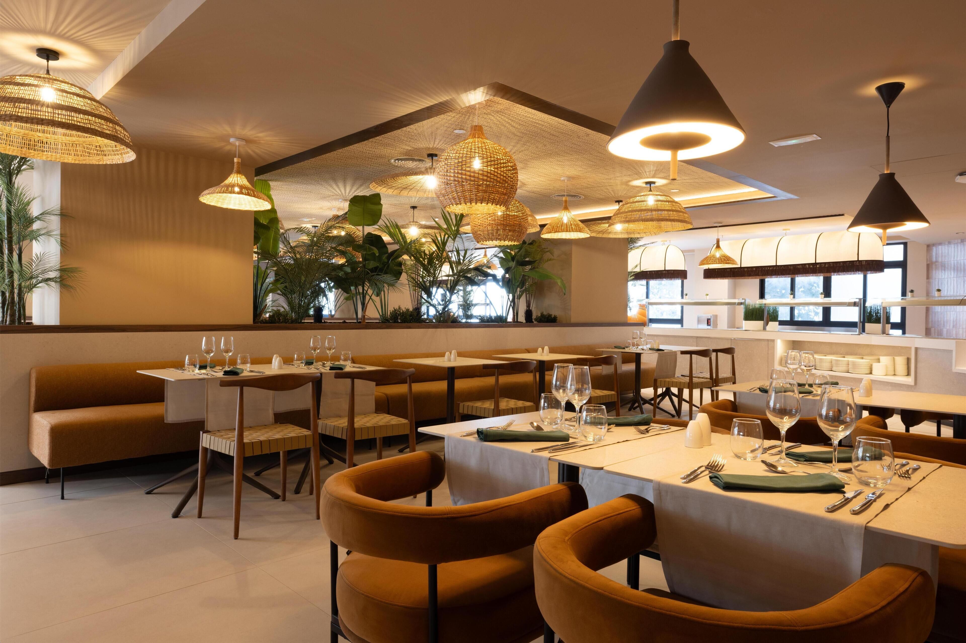 A restaurant with tables set for dining, hanging wicker lamps, and a view of the outdoors.