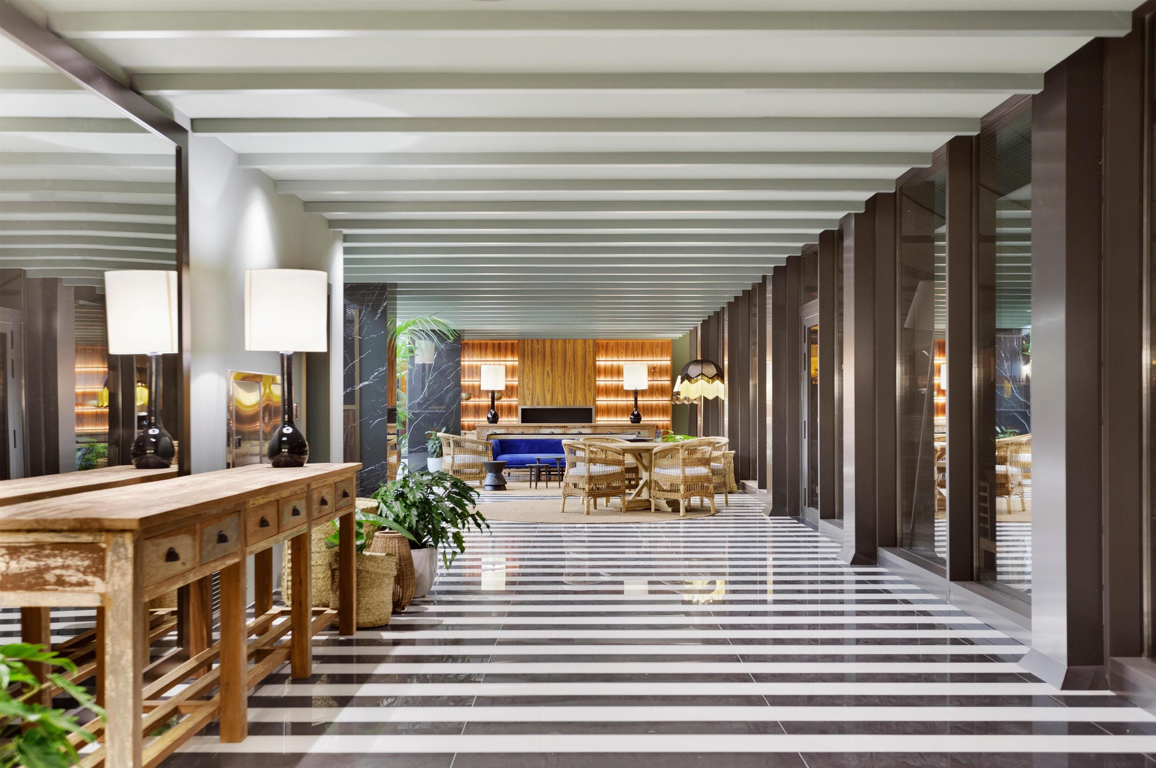 En modern hotellobby med ett rutmönstrat golv, trämöbler och en central sittgrupp med en blå soffa.