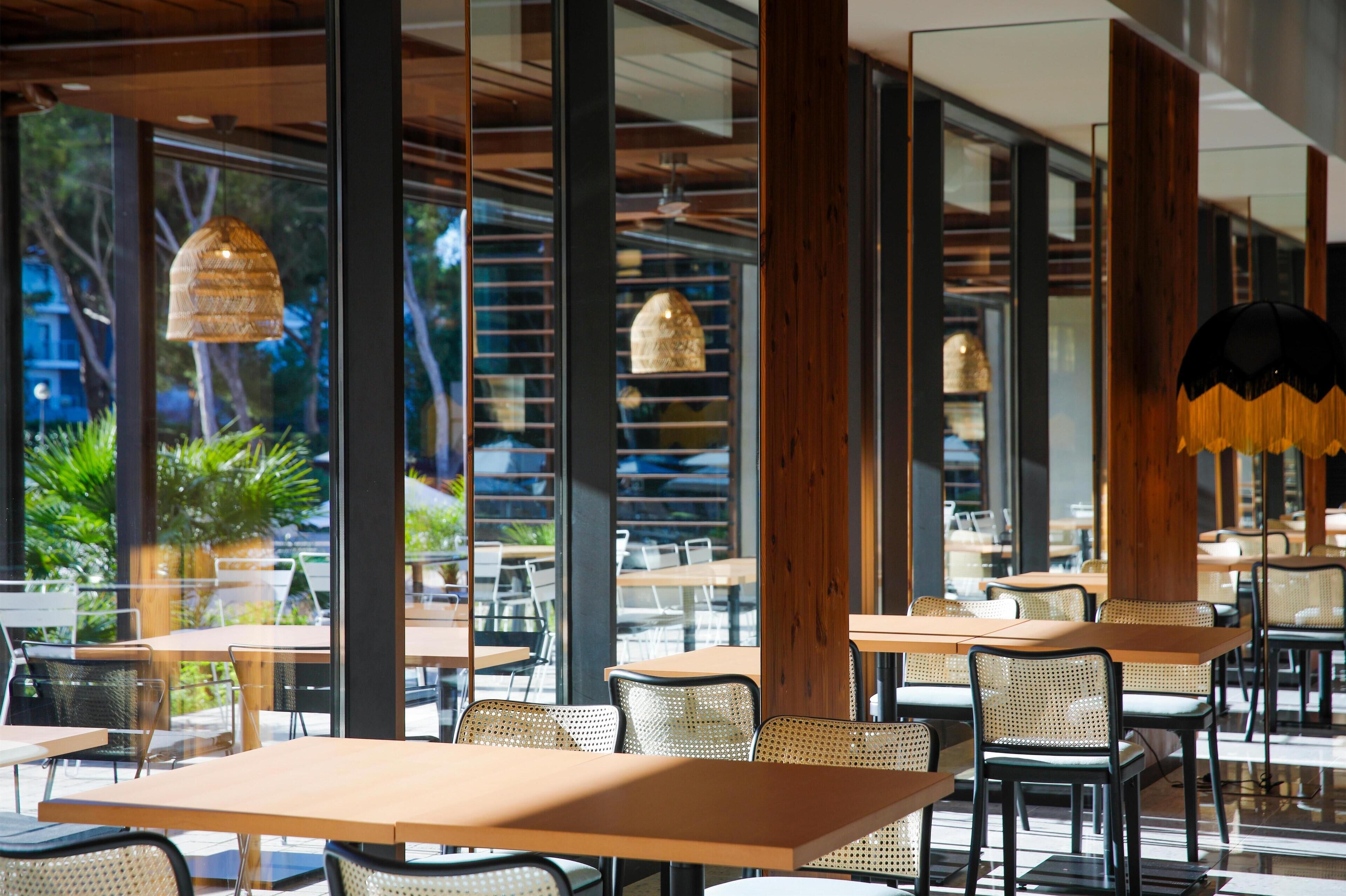 An indoor dining area with tables and chairs, large windows, and hanging pendant lights.