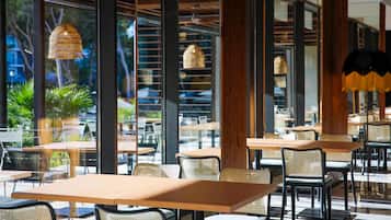 Un espace de restauration intérieur avec des tables et des chaises, de grandes fenêtres et des luminaires suspendus.