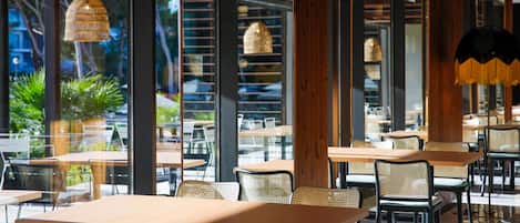 An indoor dining area with tables and chairs, large windows, and hanging pendant lights.