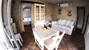Un espacio habitable compacto con una mesa de comedor, sillas blancas, un sofá y un mueble con vajilla.
