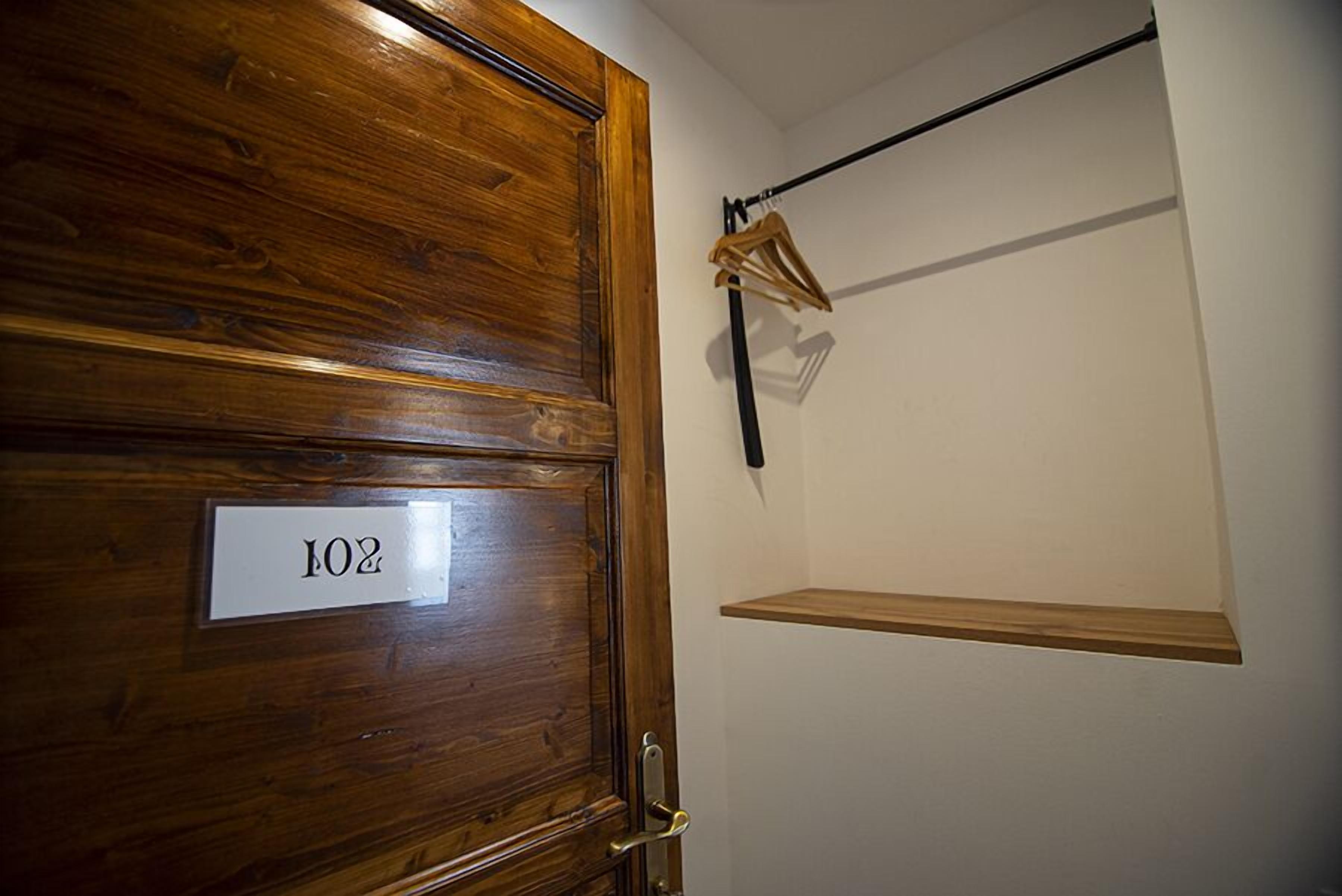 Una puerta de madera con una placa de número, un perchero y una pequeña estantería.