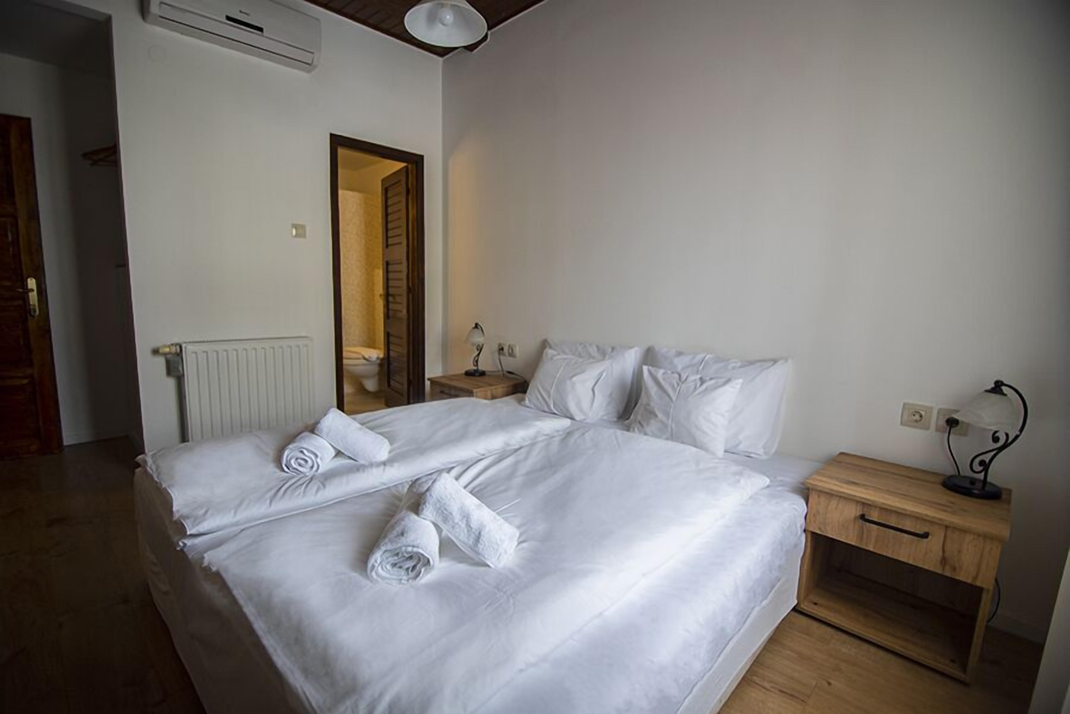 Una cama doble con sábanas blancas, una mesita de noche de madera con lámpara y un radiador en la pared.
