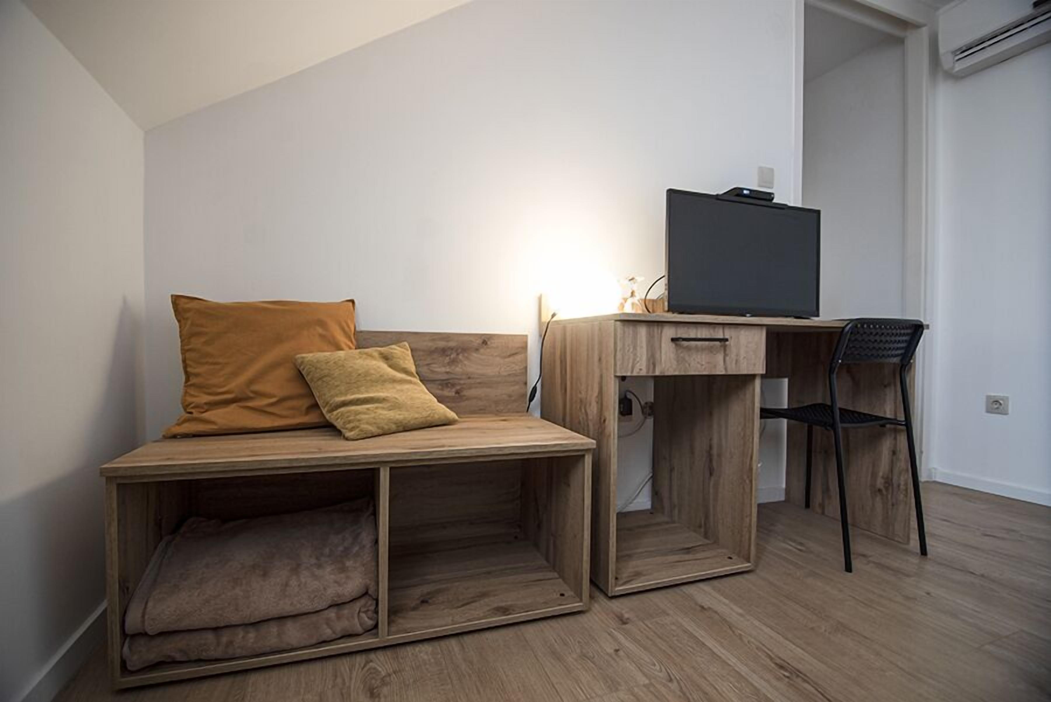 Una stanza compatta con una scrivania in legno, una sedia, una televisione e un angolo salotto con divanetto.