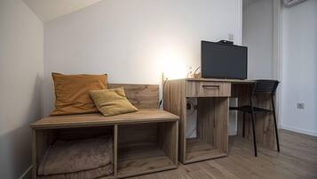 Una stanza compatta con una scrivania in legno, una sedia, una televisione e un angolo salotto con divanetto.