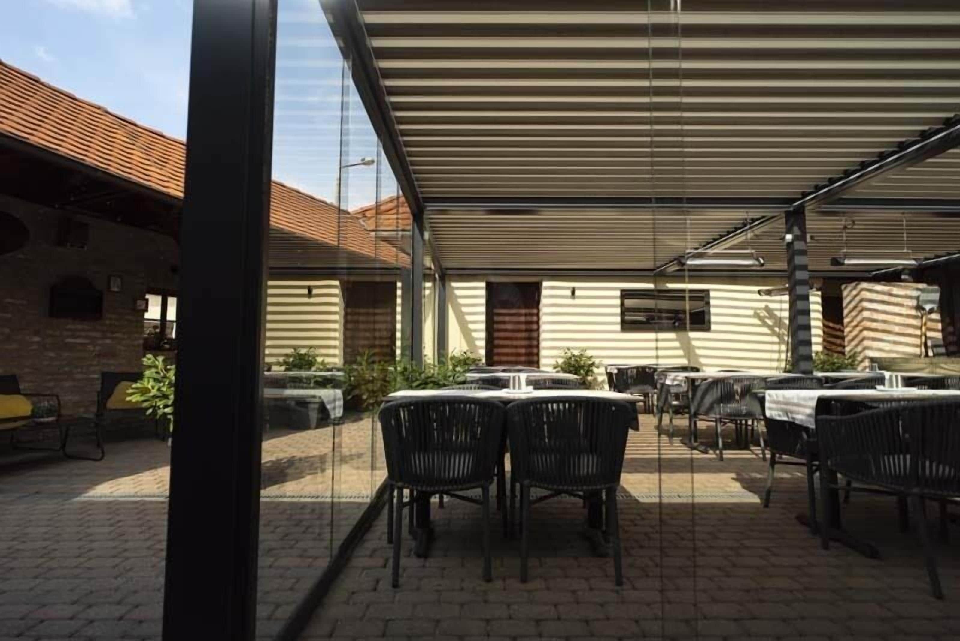 An outdoor patio with tables and chairs, a covered area, and a brick building in the background.