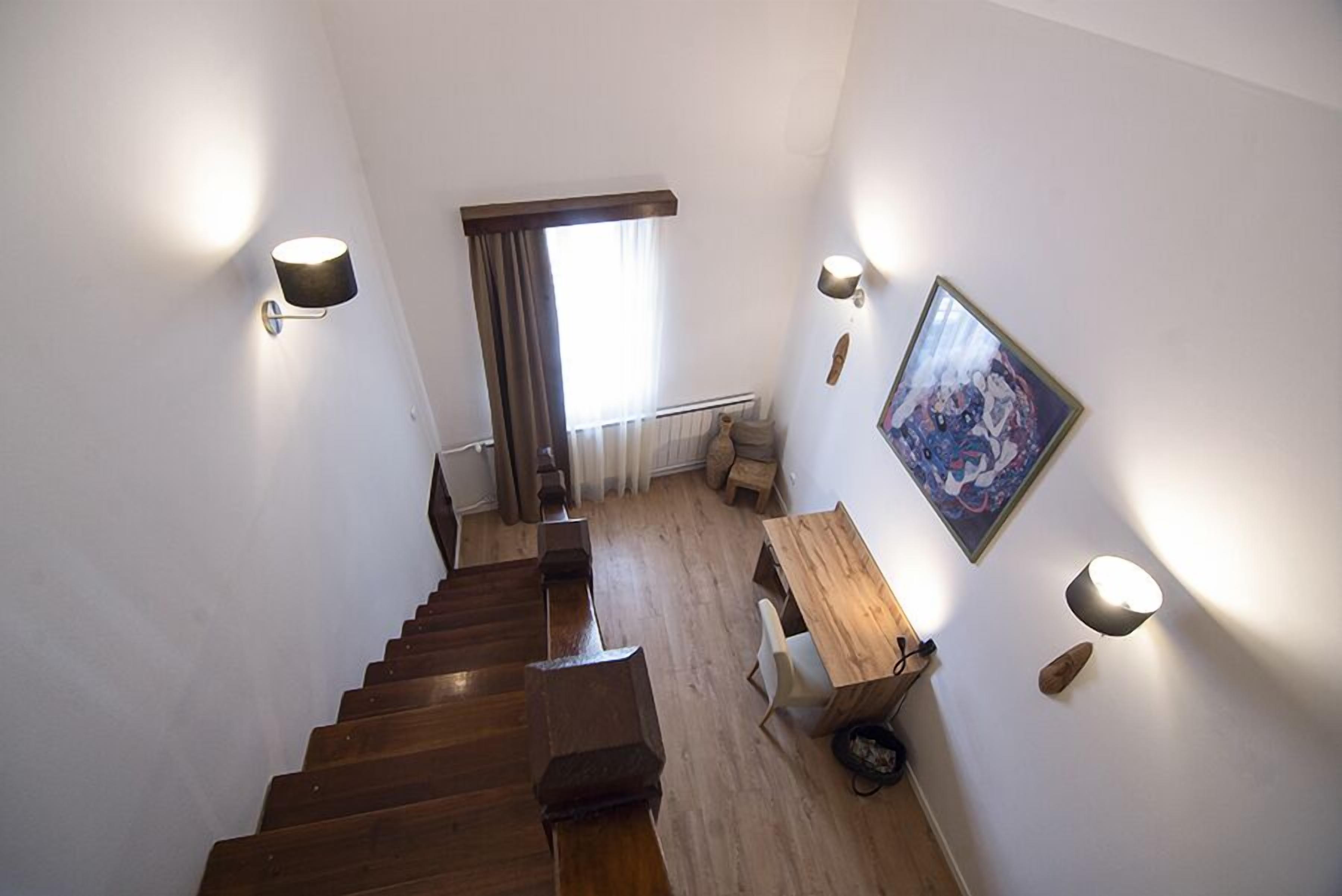 Un escalier mène à une pièce dotée d’un plancher en bois, d’un bureau, d’une chaise, d’une lampe et d’un tableau encadré accroché au mur.