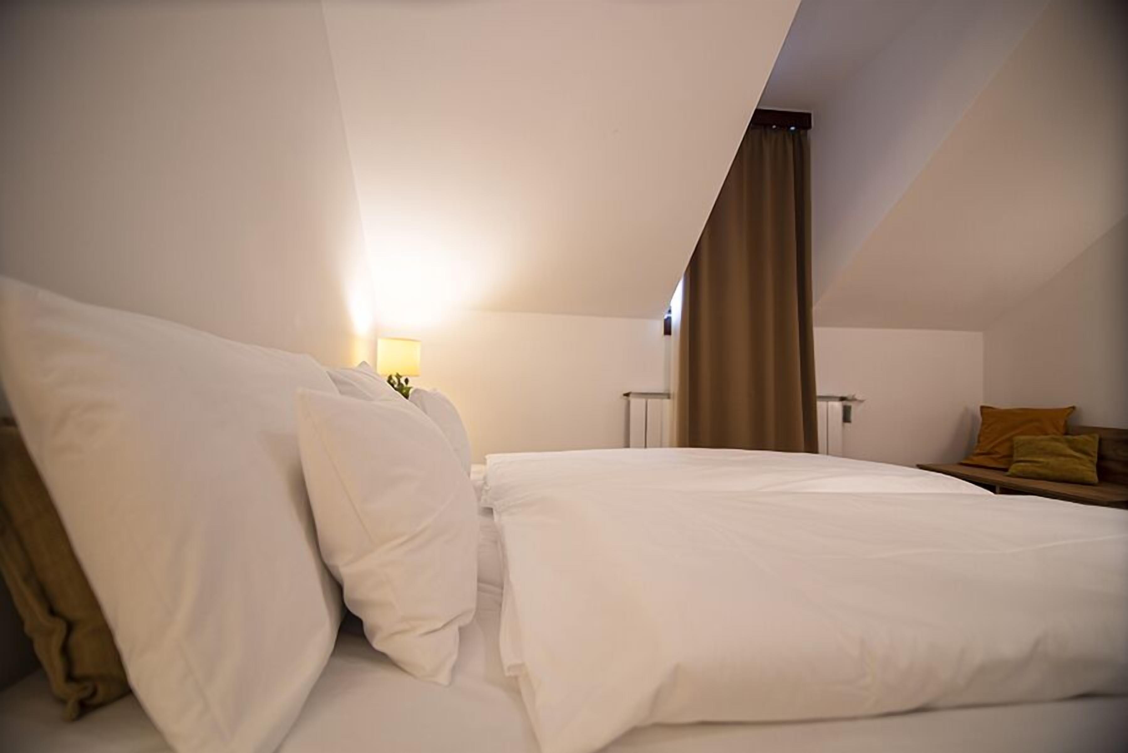 Een hotelkamer met een bed, nachtkastje, lamp en een raam met gordijnen.