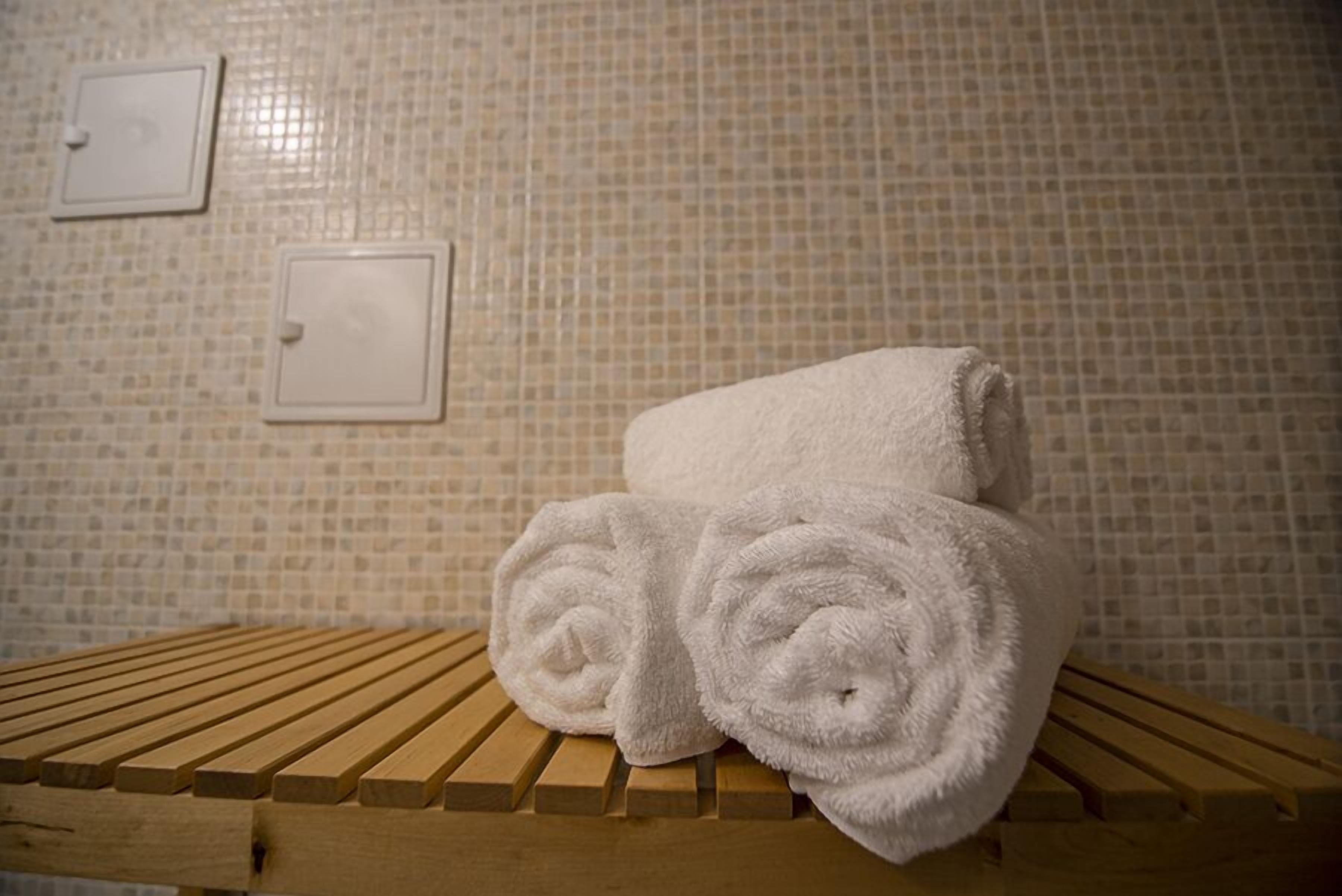 A wooden bench with two rolled white towels placed on it.