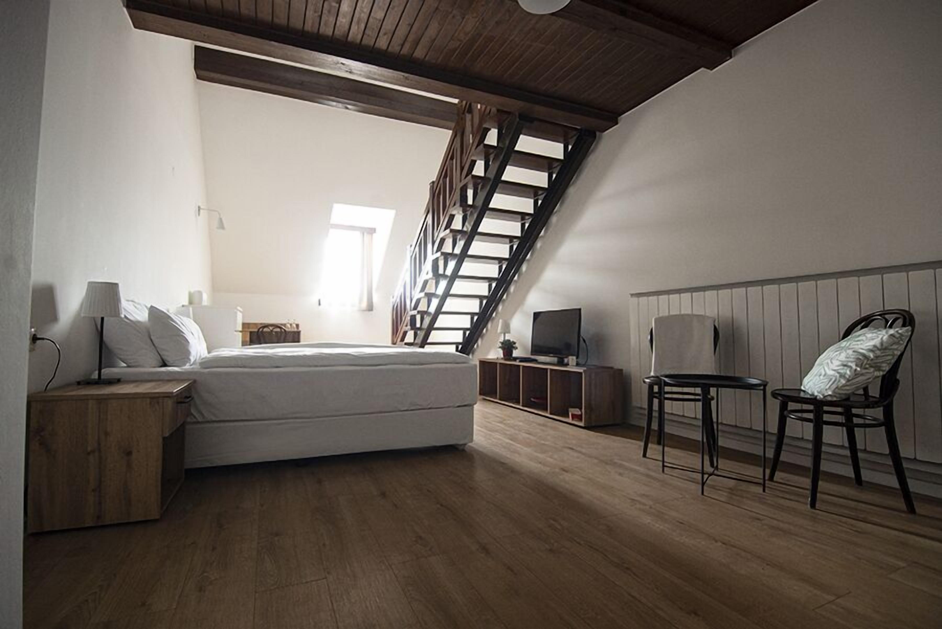 Un dormitorio con cama, mesitas de noche, televisión, una silla y una escalera de madera.