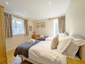 A bedroom with two beds, a bedside table, a lamp, and a window with curtains.