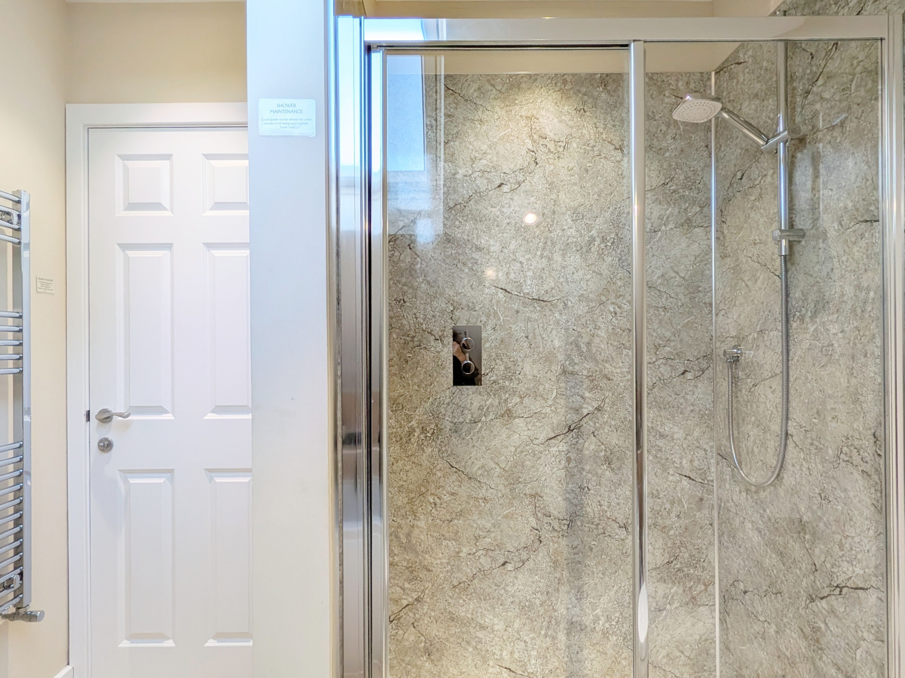 A shower with a glass door, a marble wall, and a showerhead.