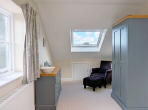 A room with a skylight, a window, a dresser, a chair, and a wardrobe.