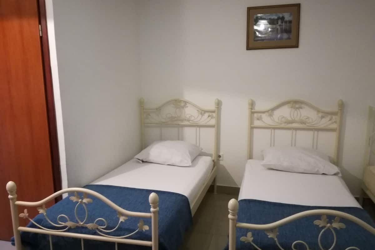 Dos camas individuales con cabeceros blancos y colchas azules en una habitación con paredes blancas y una puerta de madera.