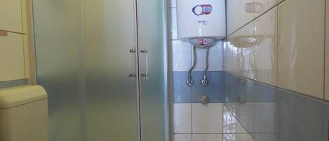 Un baño con inodoro, ducha con mampara de vidrio y calentador de agua.