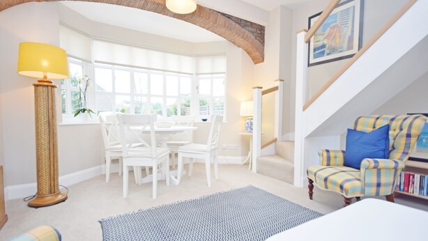 A cozy living room with a dining area, a staircase, and a view of the outdoors.