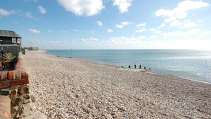 A pebbled beach with a building on the left and a clear sky.
