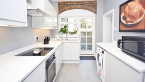 A modern kitchen with white cabinetry, a built-in oven, a microwave, and a large window with a view of the outdoors.
