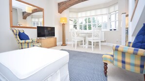 A modern living room with a flat-screen TV, a dining table with chairs, a sofa, and a patterned rug.