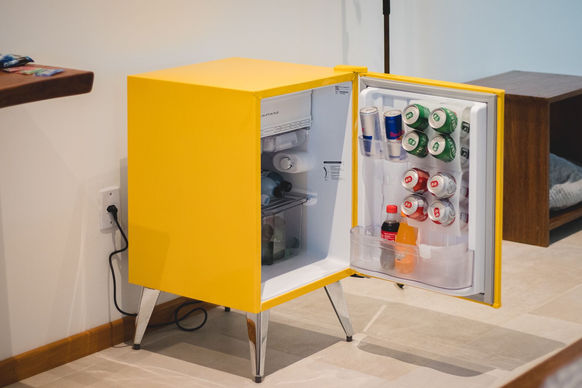 Un refrigerador amarillo pequeño con un compartimento congelador, que contiene diversas bebidas y una botella de jugo de naranja.