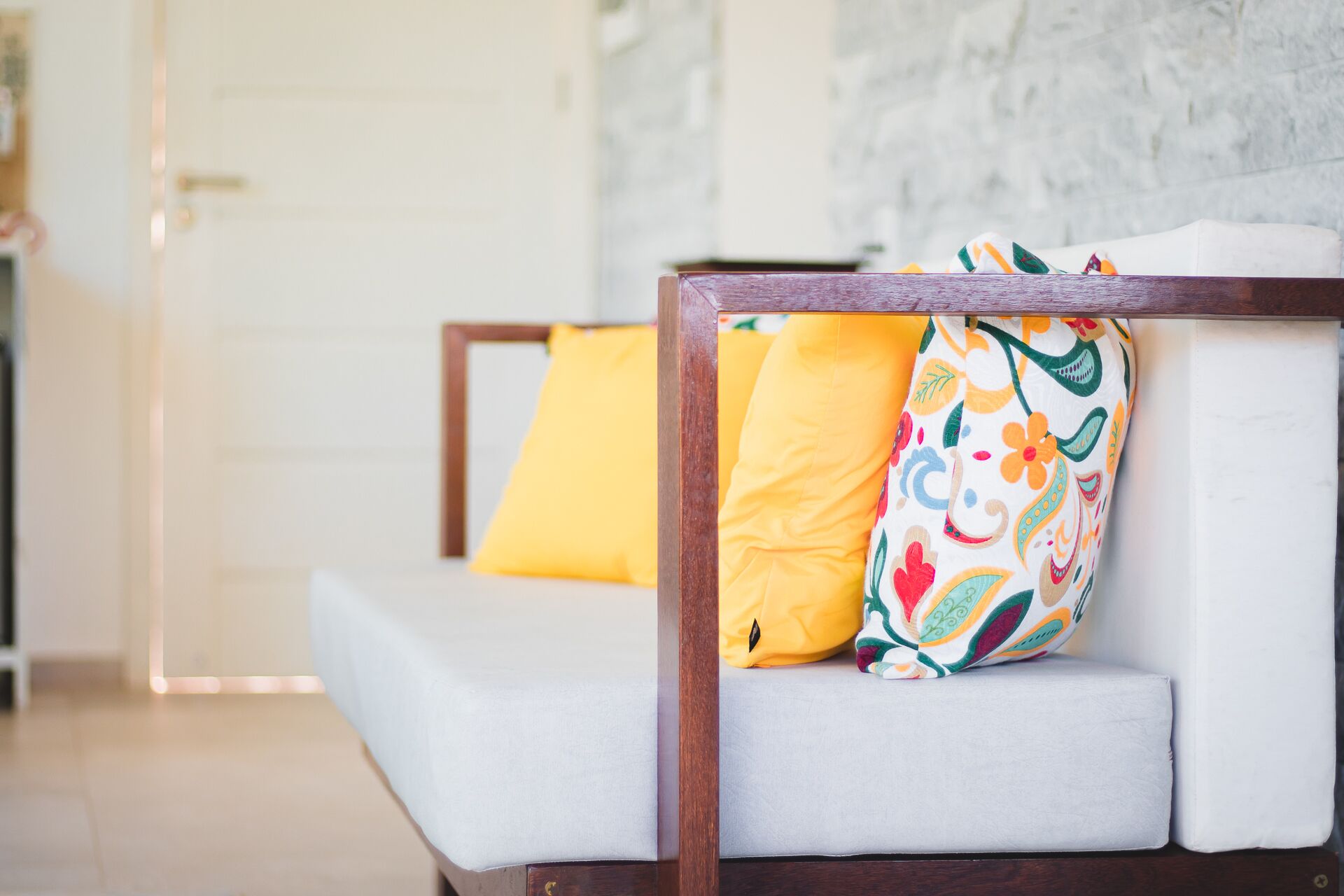 Un salon moderne avec un canapé à ossature en bois, un coussin blanc et des coussins décoratifs aux couleurs vives.