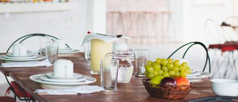 Une table à manger dressée avec des assiettes, des verres, un pichet et un panier de fruits.