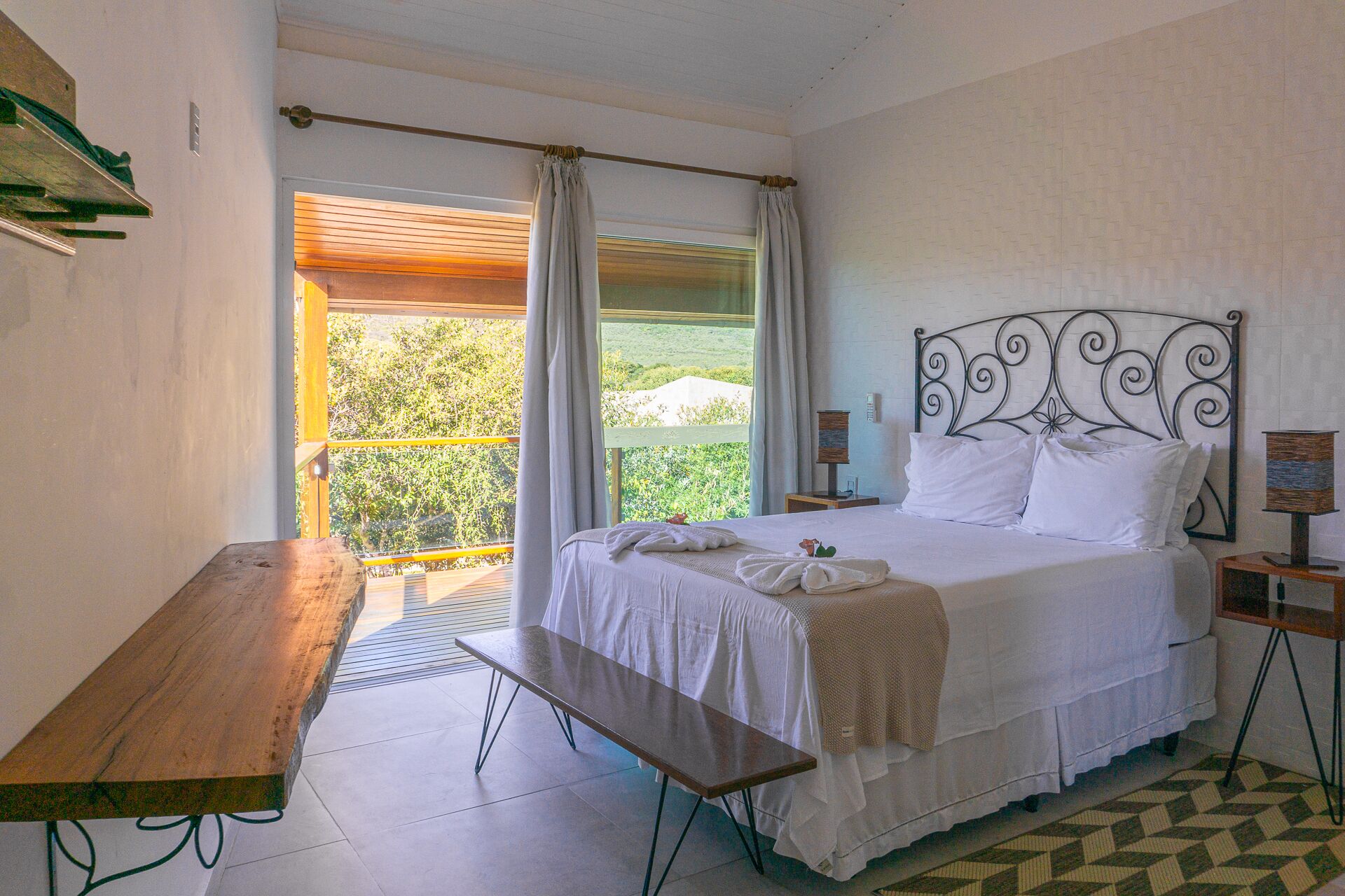 Un dormitorio con cama, banco, mesa y vistas a zonas verdes.
