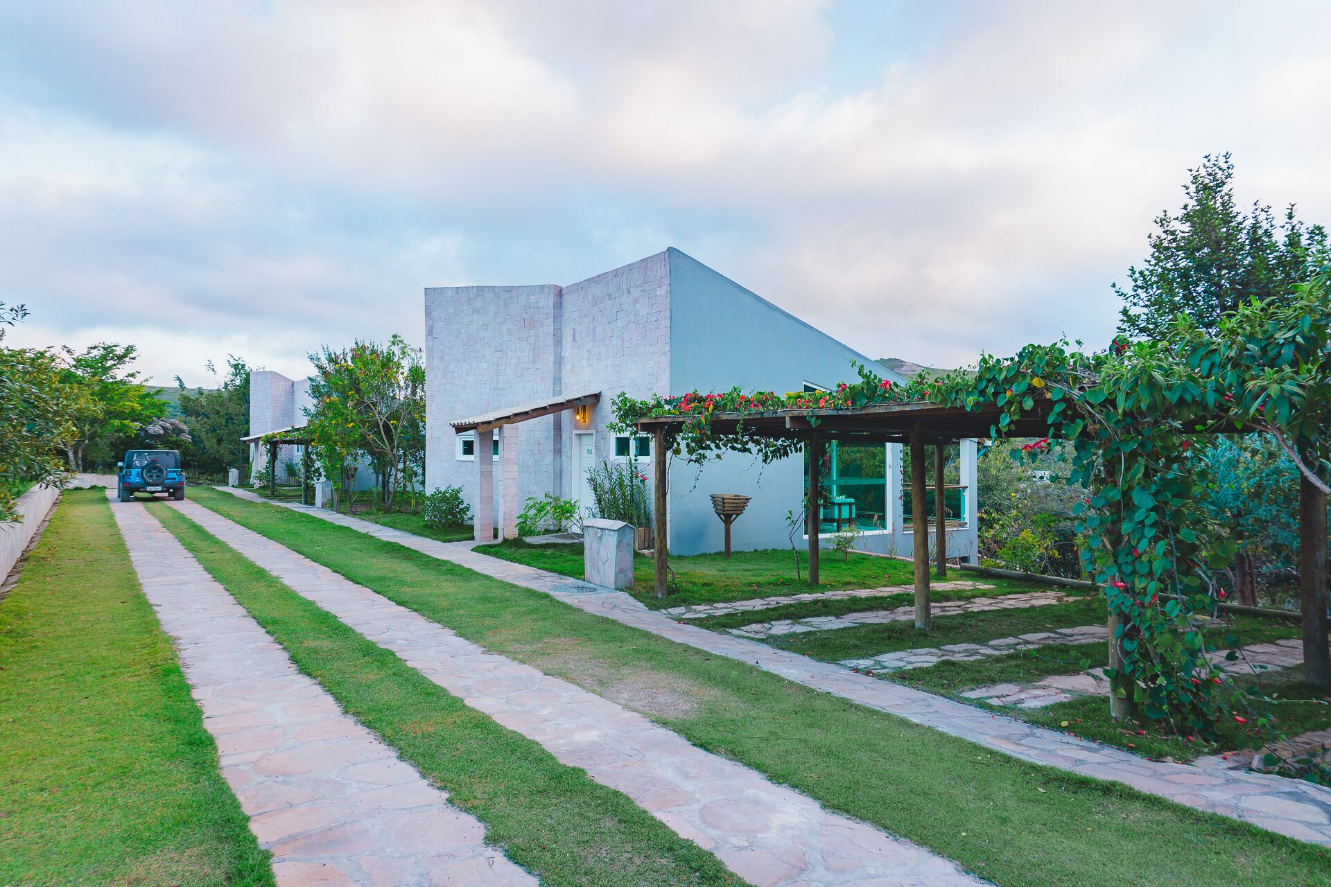 A modern house with a stone pathway, a car parked outside, and a garden with a pergola.