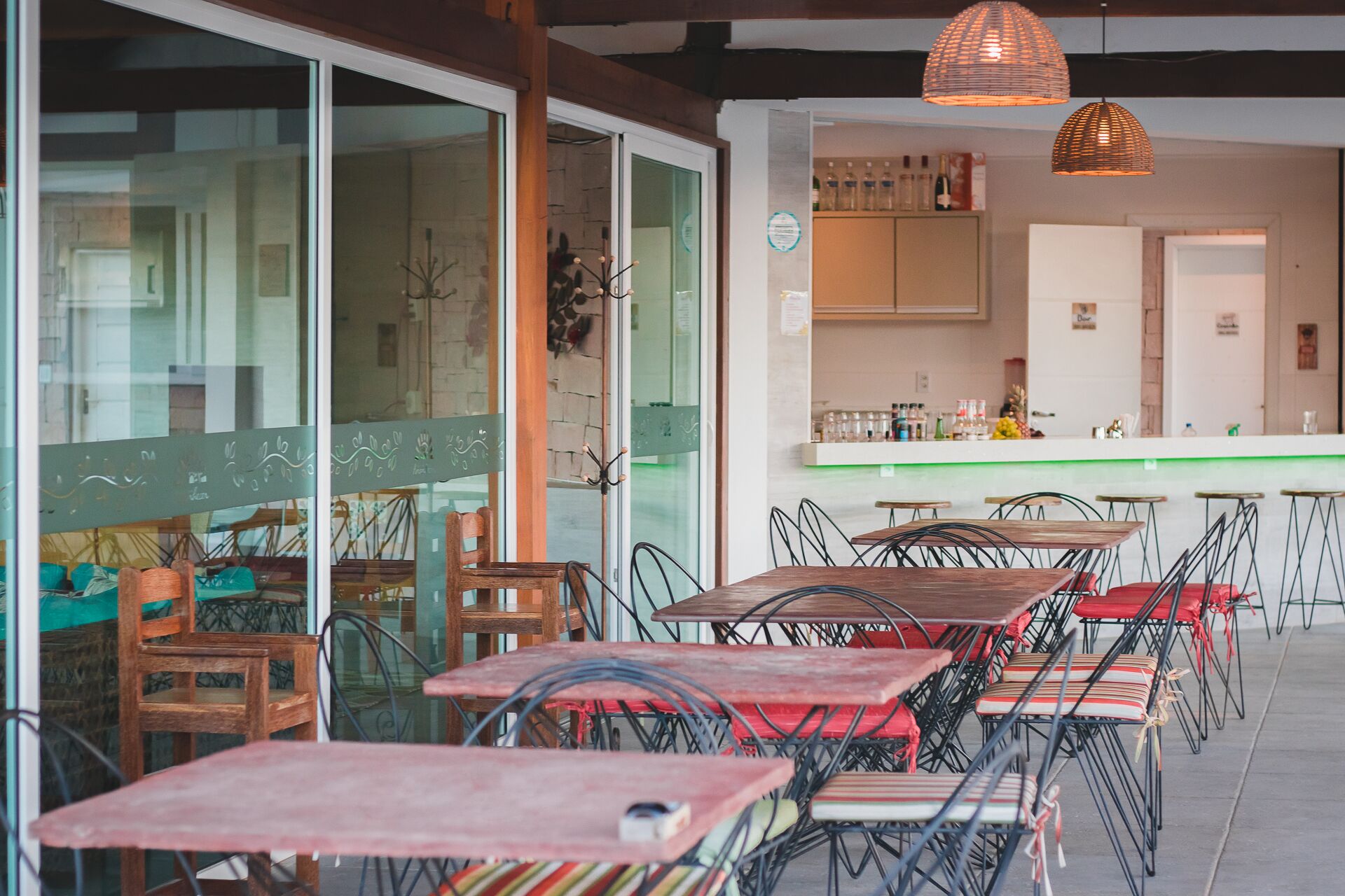 An indoor dining area with tables and chairs, a kitchen in the background, and a glass wall with decorative elements.