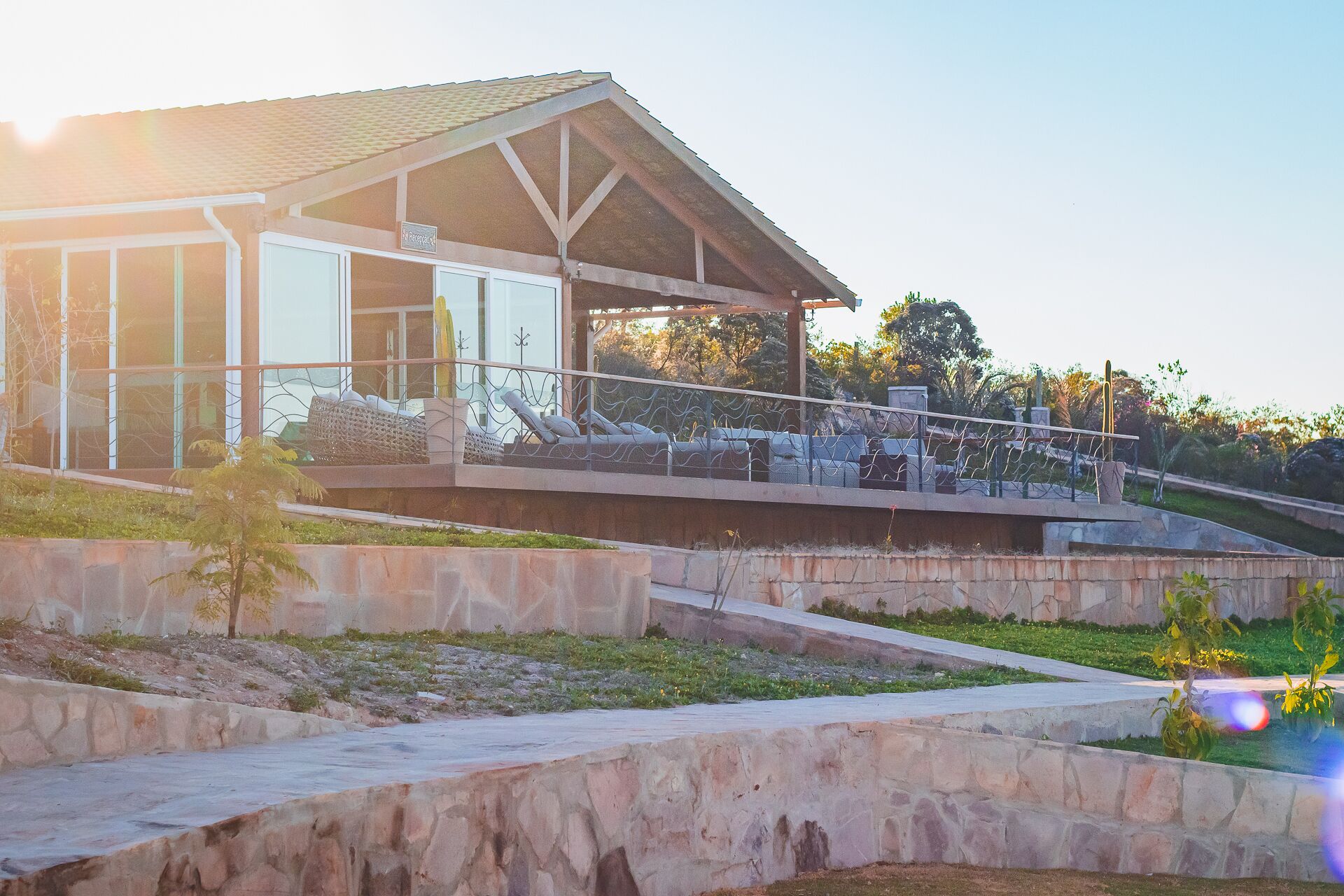 Un edificio moderno con un patio cubierto, muros de piedra de contención y un sendero que conduce a la entrada.