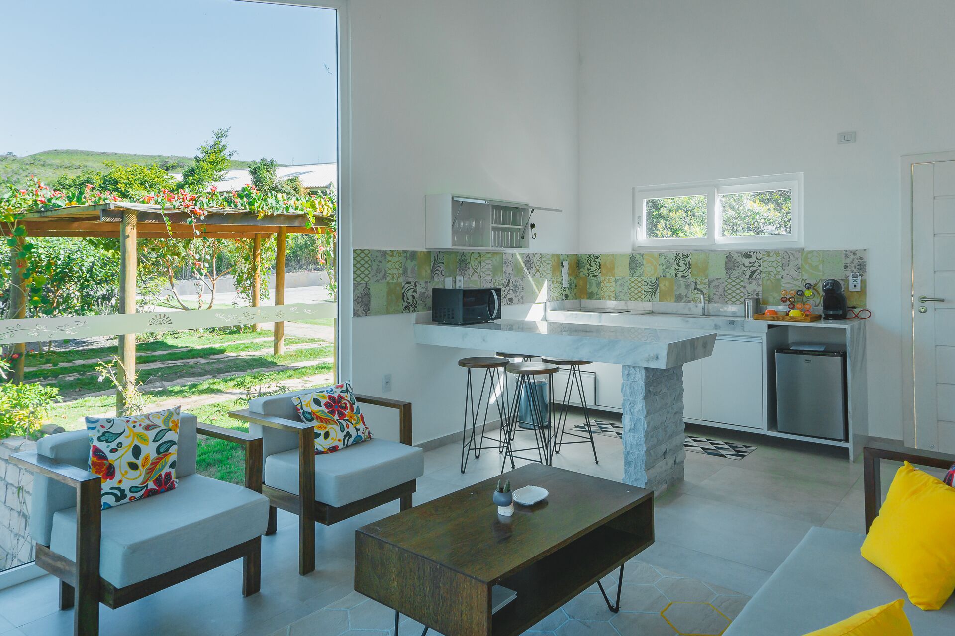A modern kitchen with a dining area, large windows, and a view of a garden.