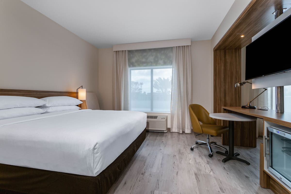 Una habitación de hotel con una cama grande, un escritorio con silla, un televisor y una ventana con cortinas.