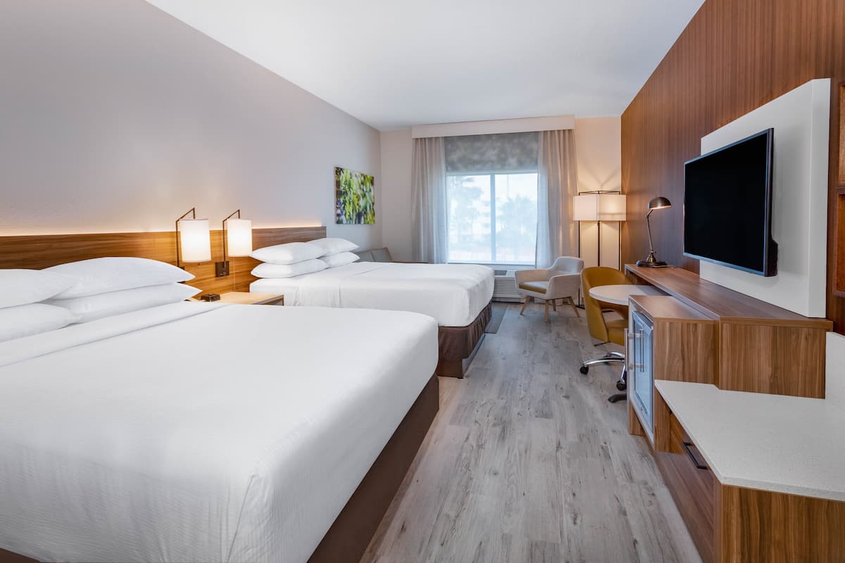 Habitación de hotel con dos camas, un escritorio, una silla, un televisor y una ventana con cortinas.