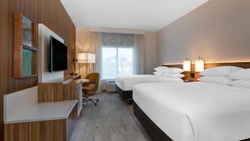 A hotel room with a flat-screen TV, a desk, two beds, a chair, and a large window with curtains.