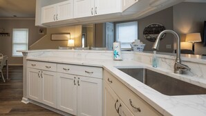 Une cuisine moderne avec des meubles blancs, un grand îlot central doté d’un évier et une horloge au mur.