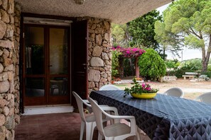 A stone-walled patio with a table set for two, surrounded by white chairs. - Casa Lisa (Olbia)